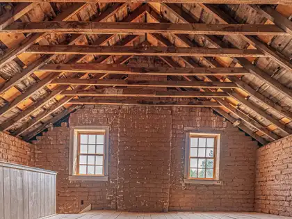 Leerer Dachboden mit Holzdachstuhl und Backsteingiebel, Licht fällt durch zwei Sprossenfenster