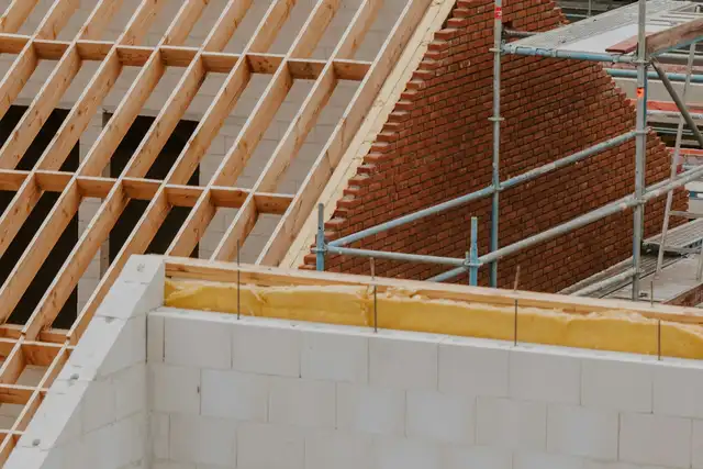 Neuer Dachstuhl aus Fichte auf einem Neubau aus Kalksandstein, mit Gerüst und Klinkergiebel