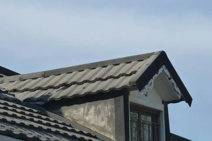 Satteldachgaube mit Holzfenster auf einem grauen Ziegeldach