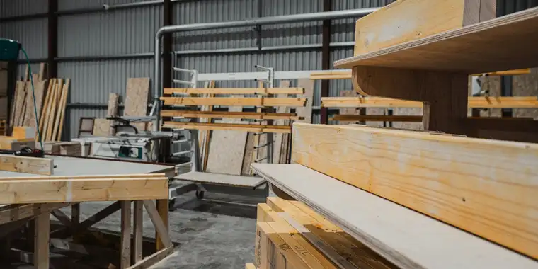 Die Halle: vorn der Zuschnitttisch und ein Stapel Bohlen, dahinter Regale mit Holz und Plattenpaketen