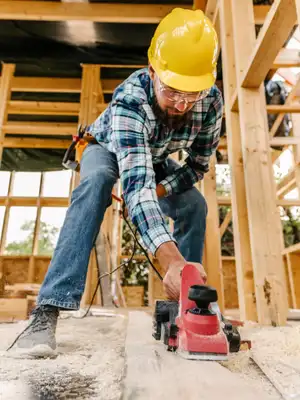 Malte mit Helm und Schutzbrille hobelt mit dem Elektrohobel ein Holz nach