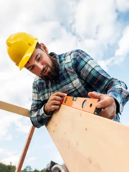 Malte mit Helm legt die Wasserwaage auf ein Holz des Dachstuhls