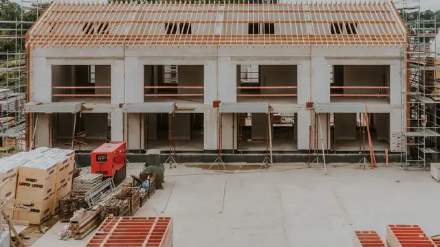 Vier Reihenhäuser im Rohbau mit fertigen Dachstühlen, davor Gerüst und Baustraße