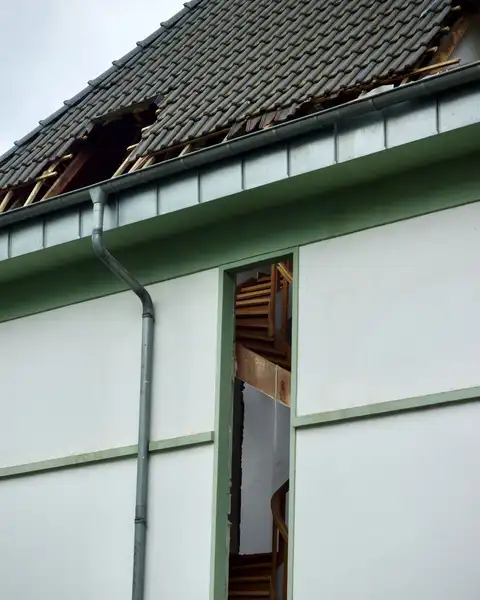Haus mit aufgerissenem Ziegeldach nach einem Sturm, die Dachlatten liegen frei