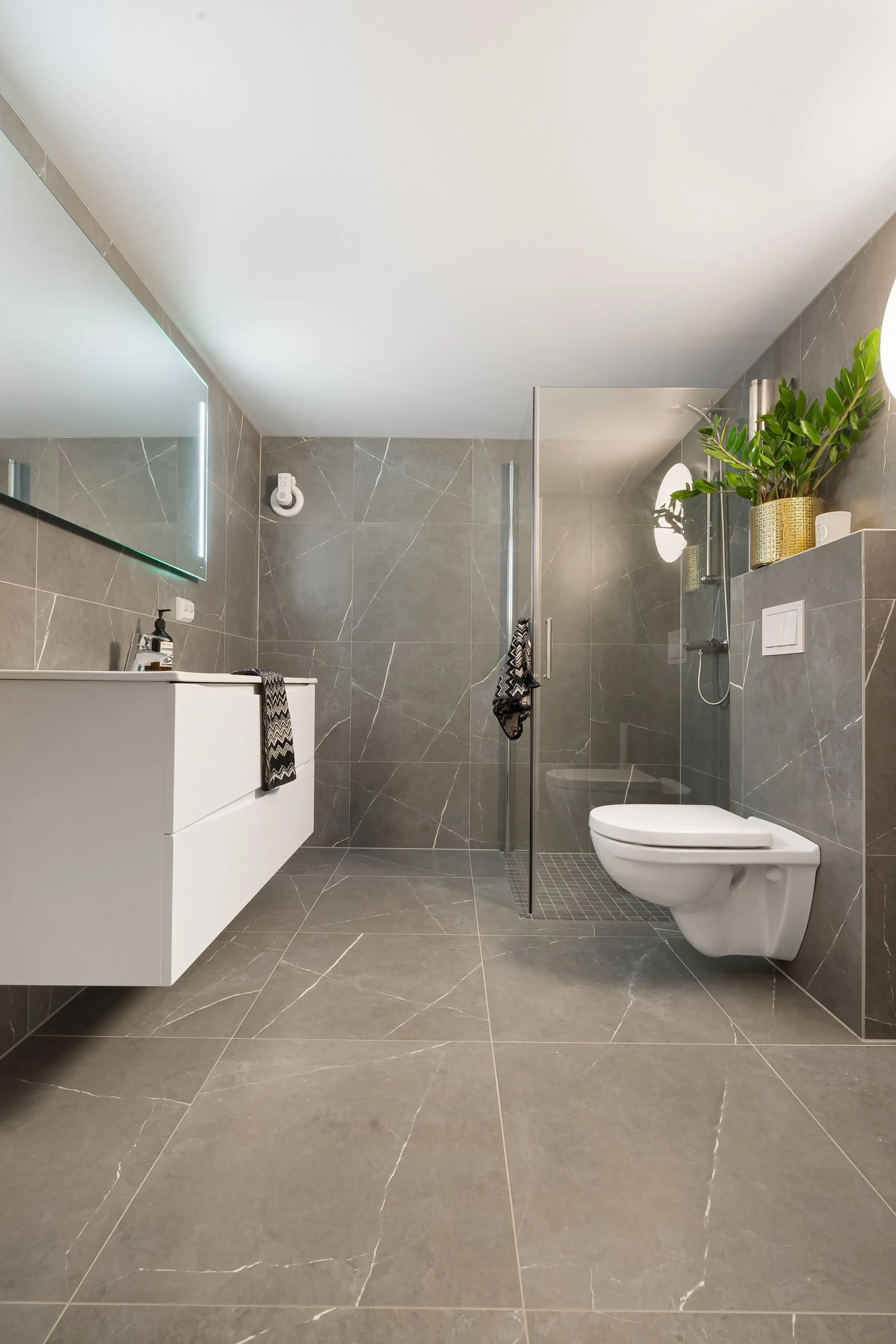 Duschbad mit Fliesen in Steinoptik: links der hängende Waschtisch, hinten Dusche und Wand-WC