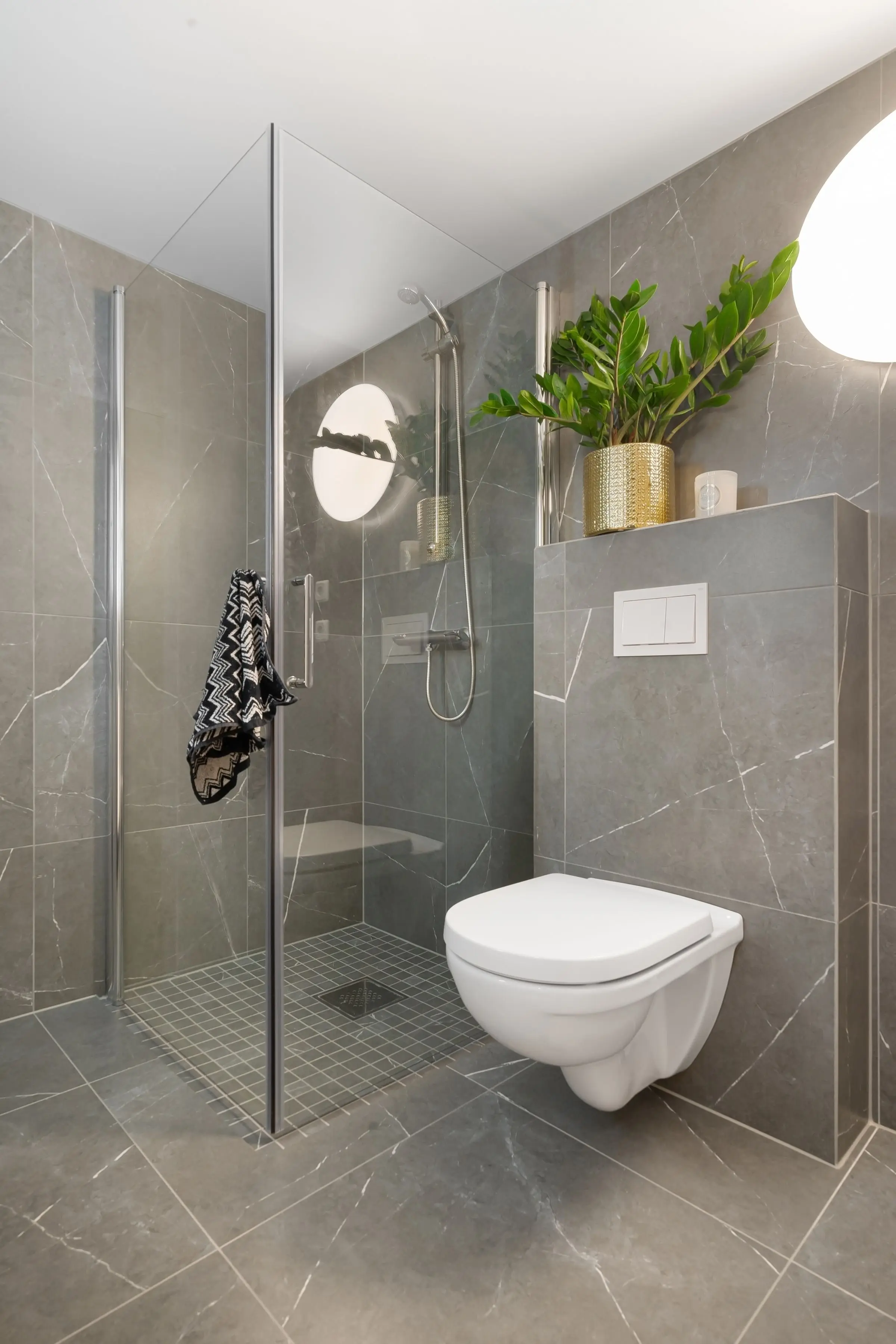 Bodengleiche Dusche mit Glastür und Mosaikboden, daneben ein Wand-WC an der Vorwand