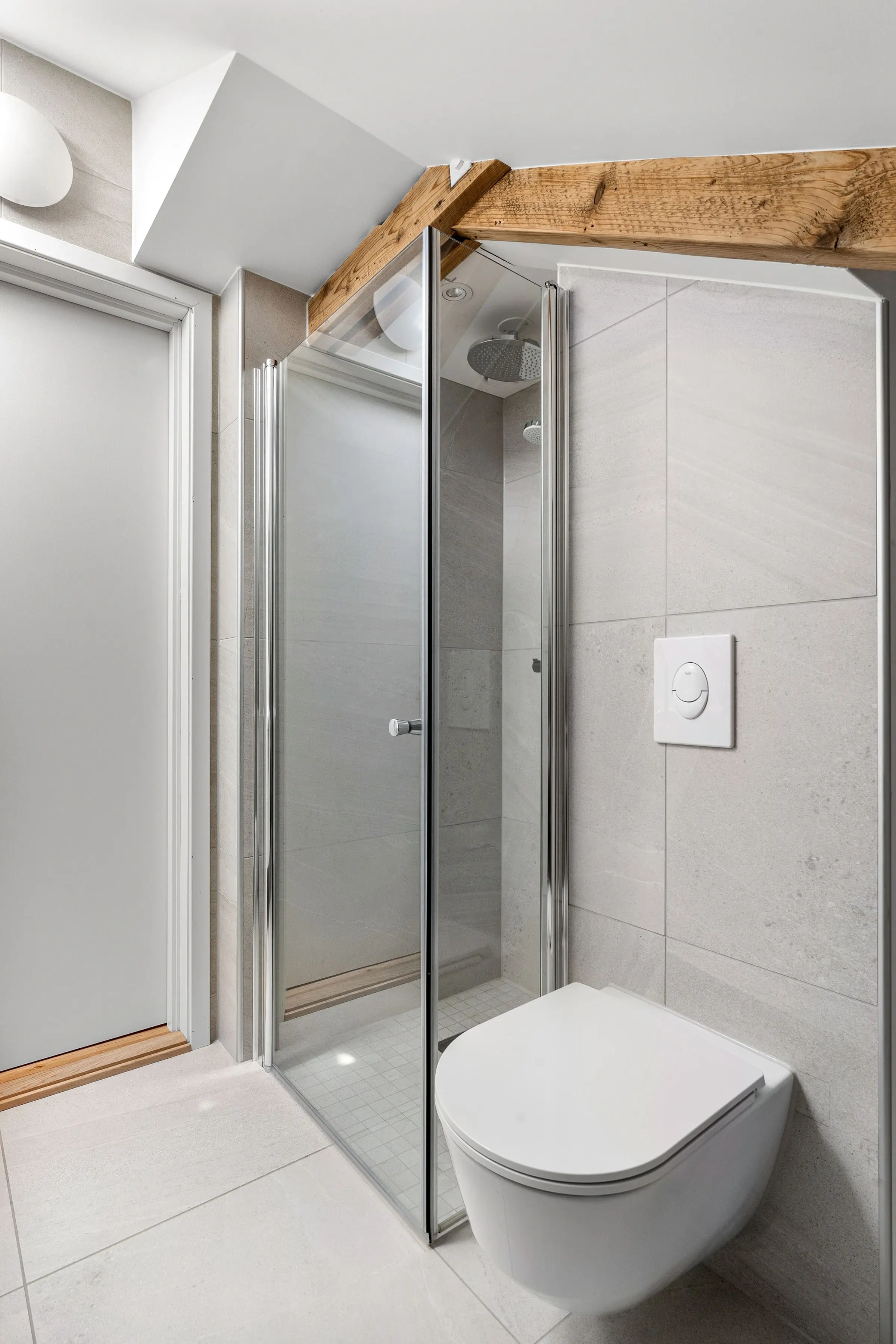 Dusche mit Glastüren unter einem Holzbalken, daneben ein Wand-WC an der Vorwand