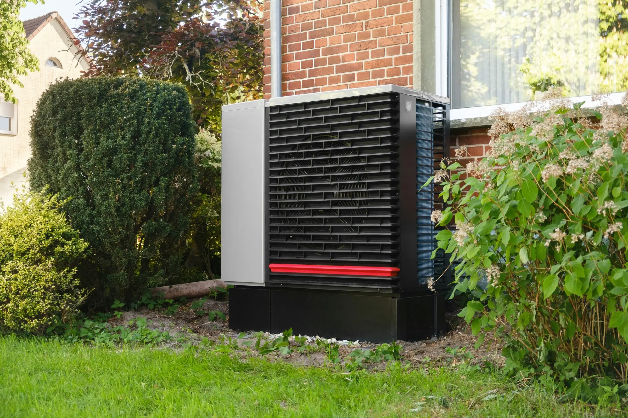 Wärmepumpe im Garten vor einem Klinkerhaus
