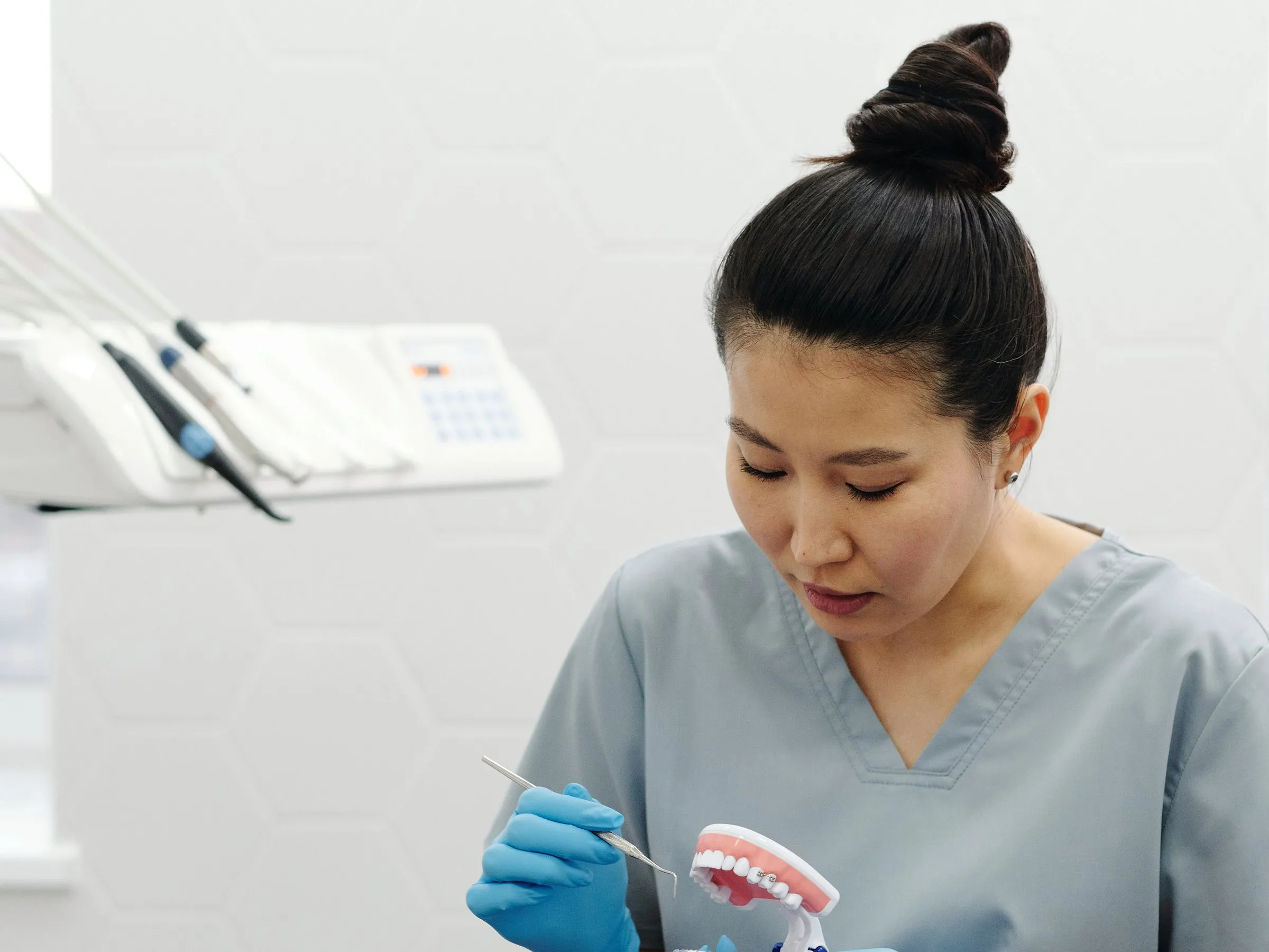 Prophylaxeassistentin in grauer Berufskleidung sitzt am Behandlungsstuhl und zeigt mit einer Sonde auf ein Kiefermodell