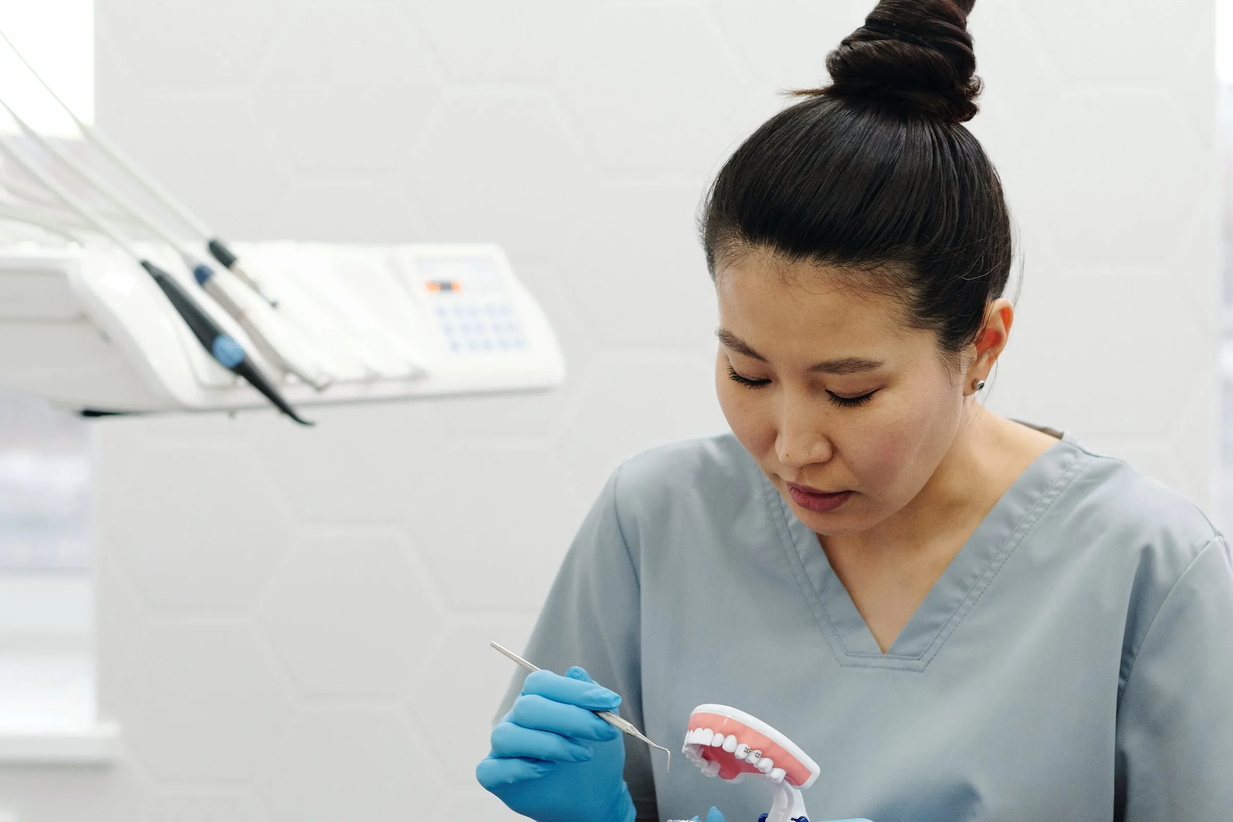 Prophylaxeassistentin in grauer Berufskleidung sitzt am Behandlungsstuhl und zeigt mit einer Sonde auf ein Kiefermodell